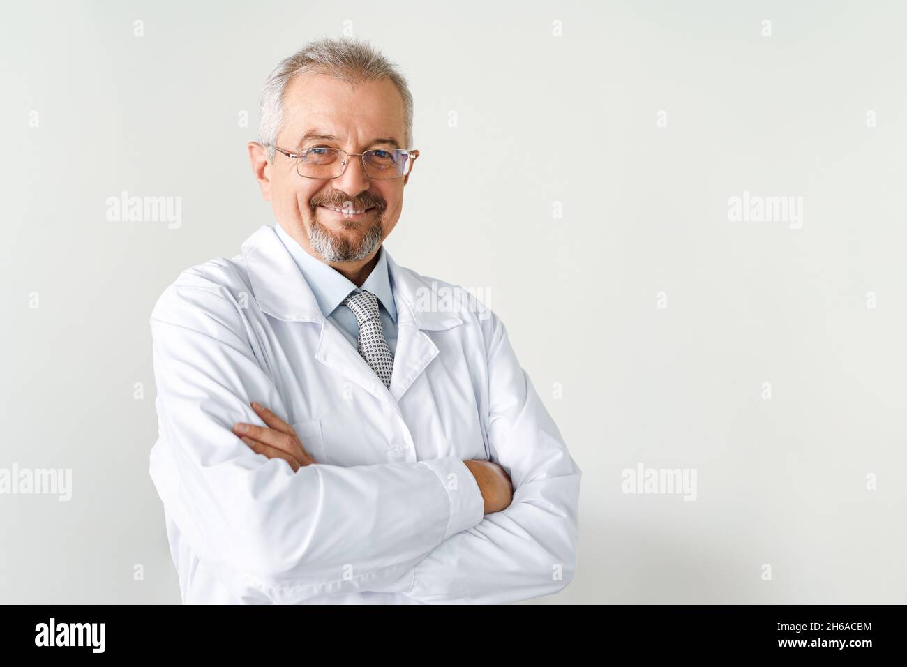 Porträt eines älteren männlichen Arztes auf weißem Hintergrund. Freundlicher Arzt, der lächelt, während er auf die Kamera schaut. Stockfoto