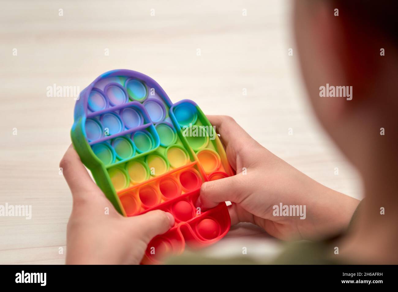 Kinder Hände schieben sensorische Pop it. Farbenfrohe Antistress-Spielzeuge, einfache Grübchen, Pop-Tube. Rainbow Silikon sensorische Fidget Neue beliebte trendige Silikon-Spielzeug. Stockfoto