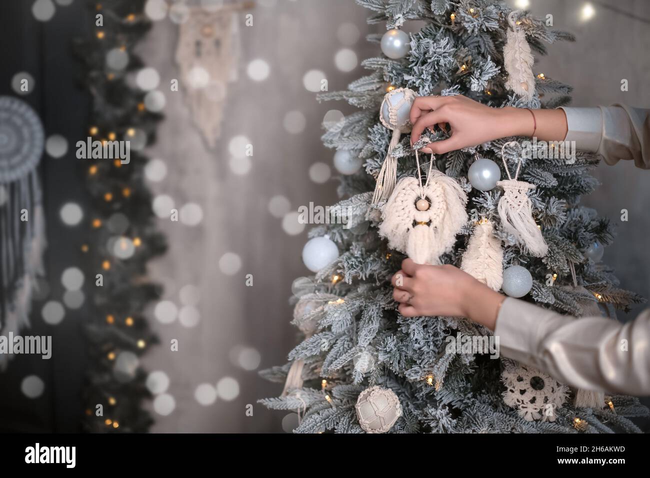 Die Hände eines Mädchens mit einem modischen makramen Weihnachtsschmuck schmücken einen Weihnachtsbaum im skandinavischen Stil. Handgefertigte Dekoration im Boho-Stil Stockfoto