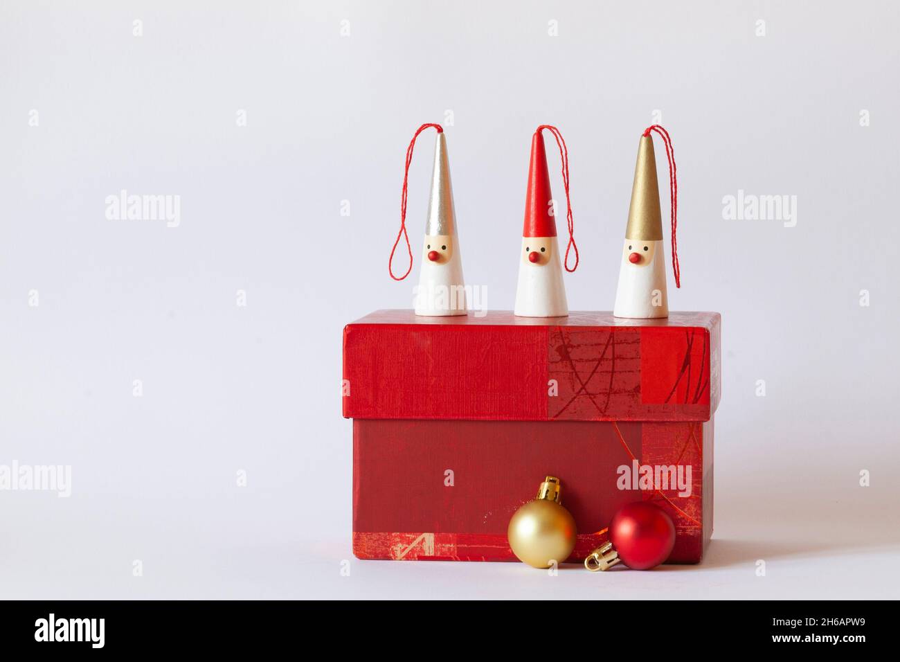 Drei Weihnachtsmänner-Figuren auf einer roten Geschenkbox, dekorative Weihnachtsbaumkugeln, weißer Hintergrund, Seitenansicht, Kopierraum Stockfoto