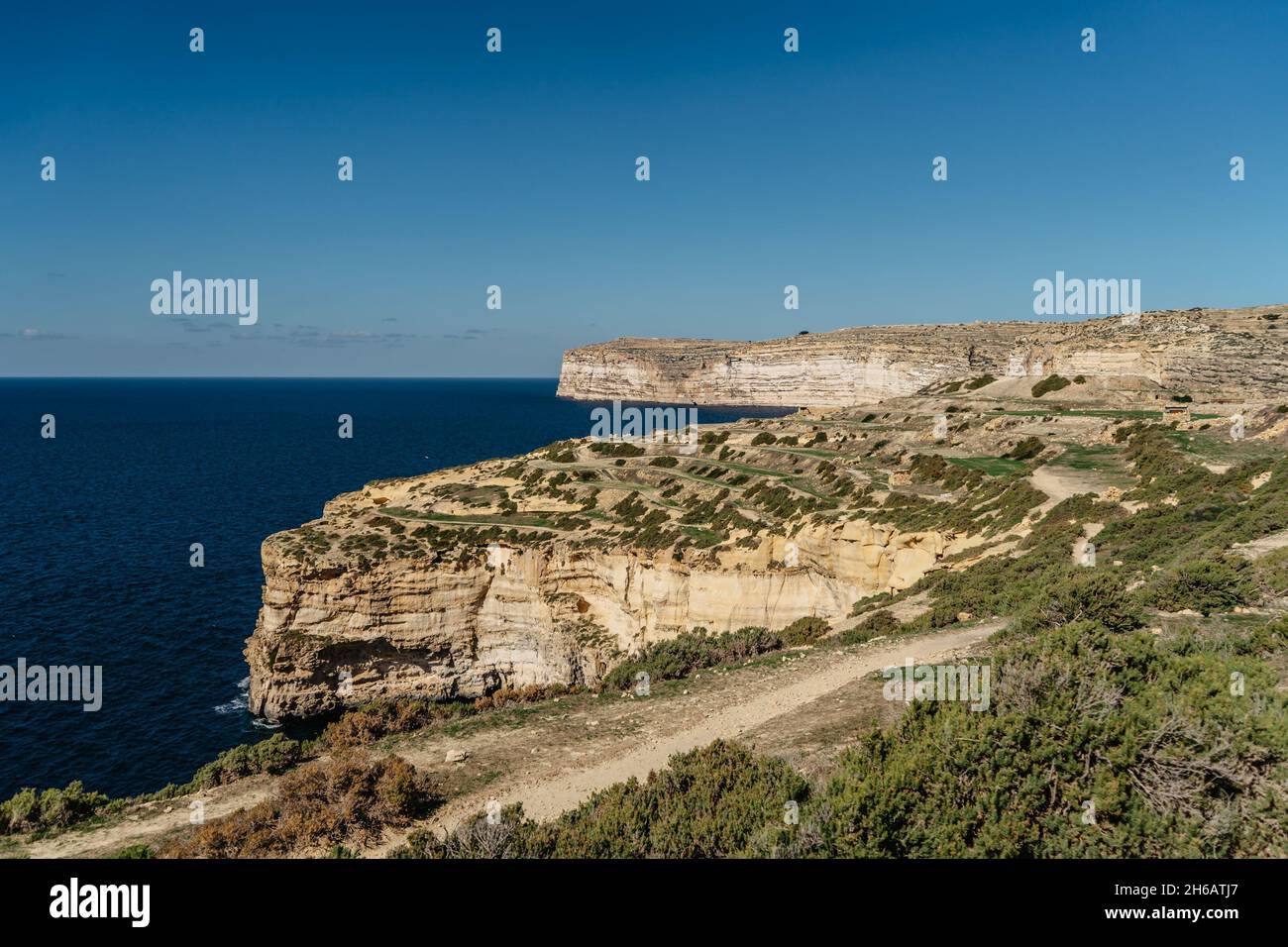Felsige Kalksteinküste der Insel Gozo und Mittelmeer mit türkisblauem Wasser und Höhlen. Grüne terrassenförmige Felder, Hügel. Beliebte Wanderklippe Stockfoto