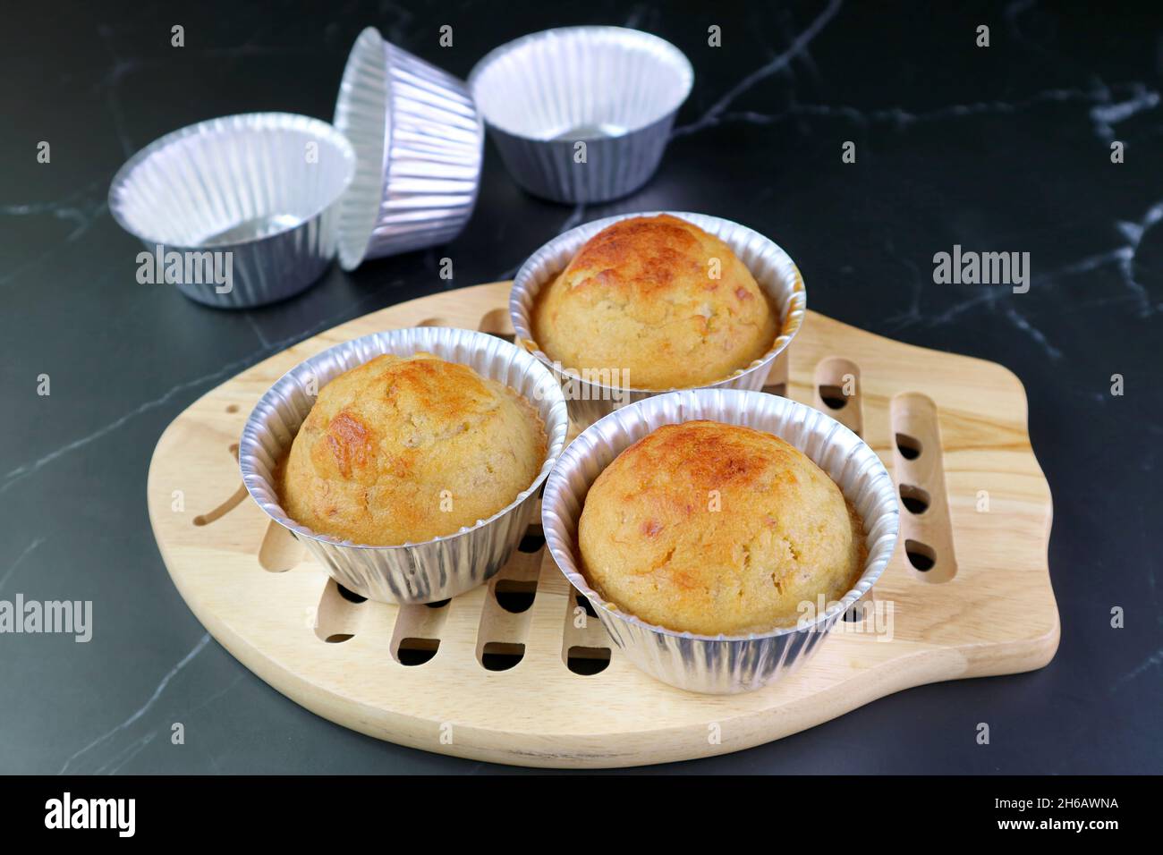 Köstliche Bananenmuffins in den Formen auf einem hölzernen Breadboard mit leeren Formen im Hintergrund Stockfoto