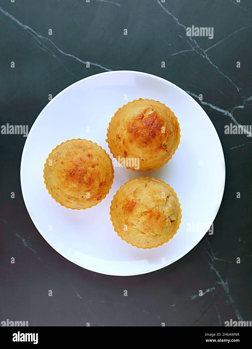 Draufsicht auf einen Teller mit Bananenmuffins auf dem Tisch aus schwarzem Marmor Stockfoto