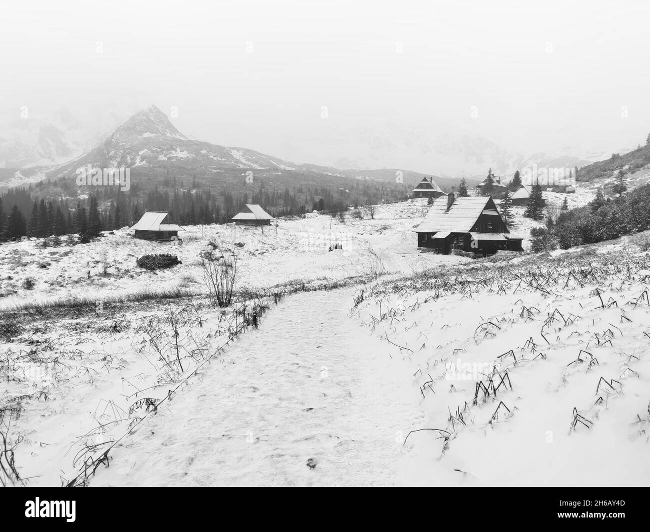 Eine graue Landschaft mit schneebedeckten Dorfhäusern und Bergen an einem nebligen Tag Stockfoto