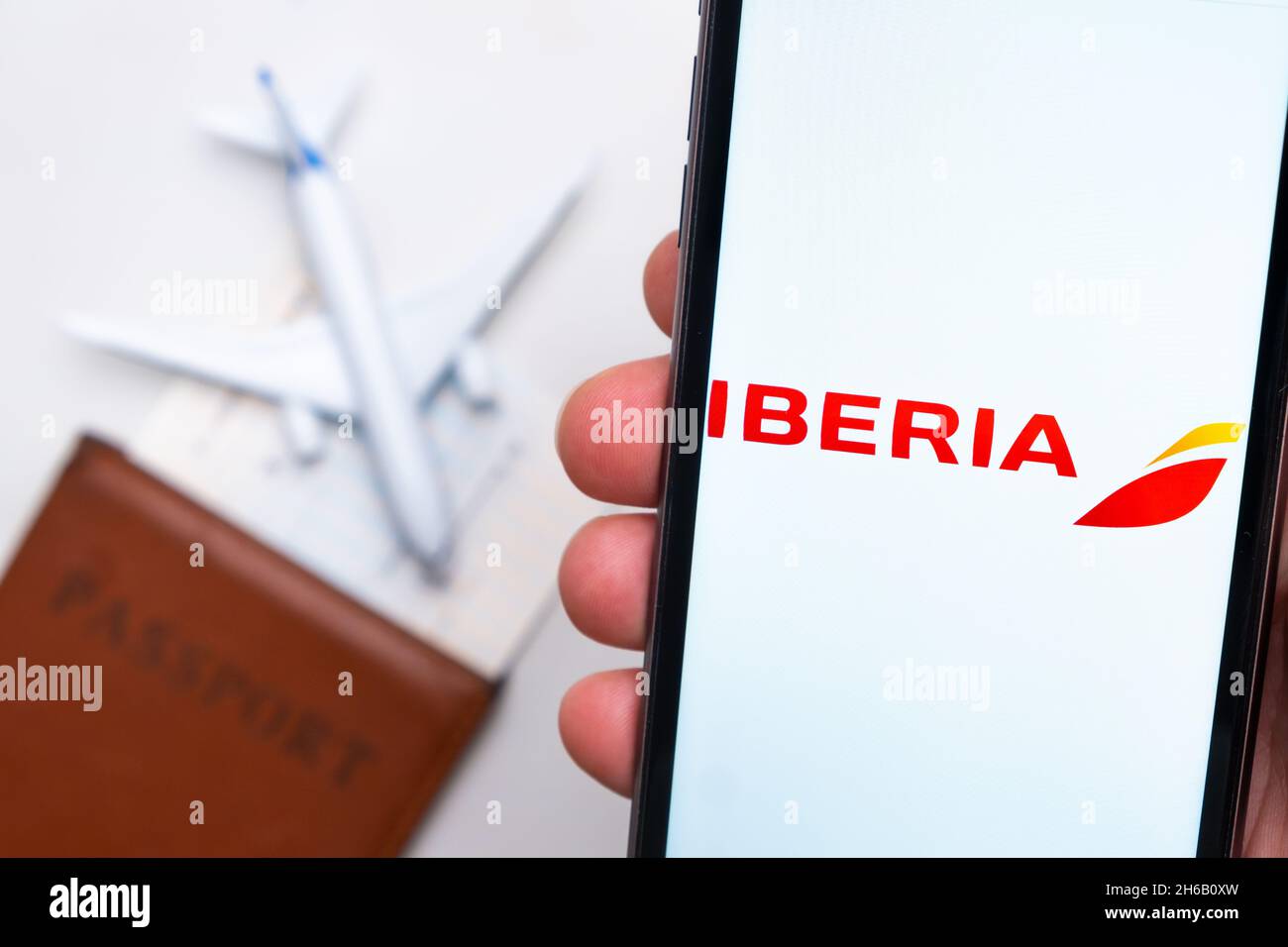 Logo des Unternehmens Iberia Airlines auf dem Handybildschirm in Menschenhand auf dem Hintergrund von Pass, Bordkarte und Flugzeug, September 2021, San Francisco, USA. Stockfoto