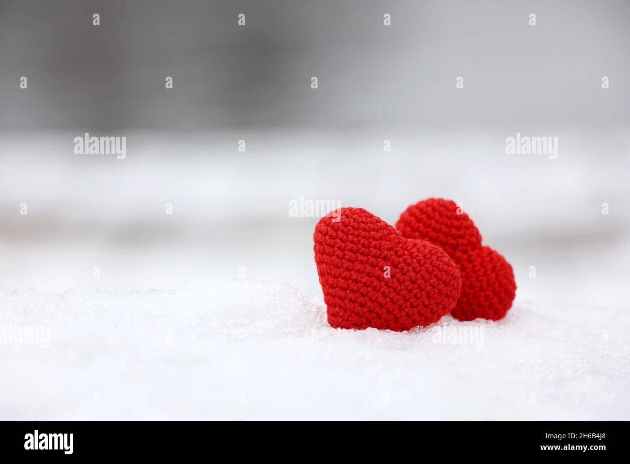 Liebe Herzen im Schnee in einem Park. Valentinskarte, zwei rote gestrickte Symbole der Liebe, Hintergrund für romantische Veranstaltung im Winter, Weihnachtsfeier Stockfoto