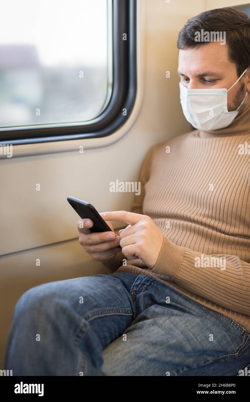 Ein Mann mit medizinischer Maske fährt in einem Zug und benutzt sein Telefon. Moskau, Russland. Stockfoto