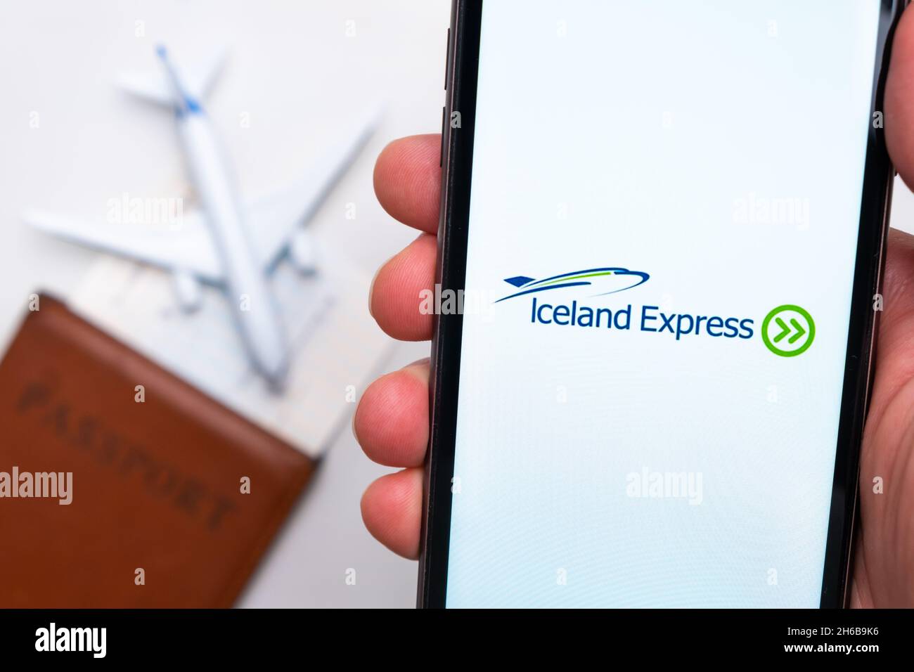 Iceland Express Anwendung auf dem Smartphone-Bildschirm mans handn. Ein weißes Spielzeugflugzeug und ein Reisepass liegen auf einem Tisch mit heller Oberfläche.November 2021, San Francisco, USA Stockfoto