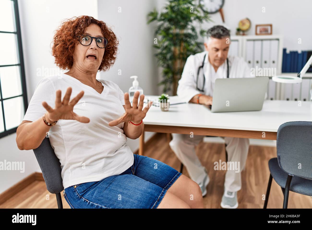 Ältere Frau sitzt bei Arzttermin Angst und erschrocken vor Angst Ausdruck Stop Geste mit den Händen, schreiend in Schock. Panik Konzept. Stockfoto