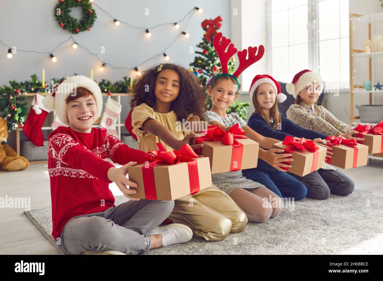 Kinder von 8-9 Jahren sitzen in einer Reihe und halten ihre Weihnachtsgeschenke vor sich. Stockfoto