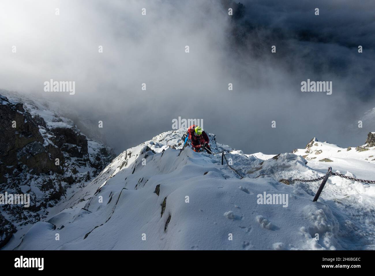 Kletterer, der auf eisigen Felsen hochklettert, während er Kette hält, über den Klettersteig in der Hohen Tatra auf dem Weg zum Rysy-Gipfel. Stockfoto