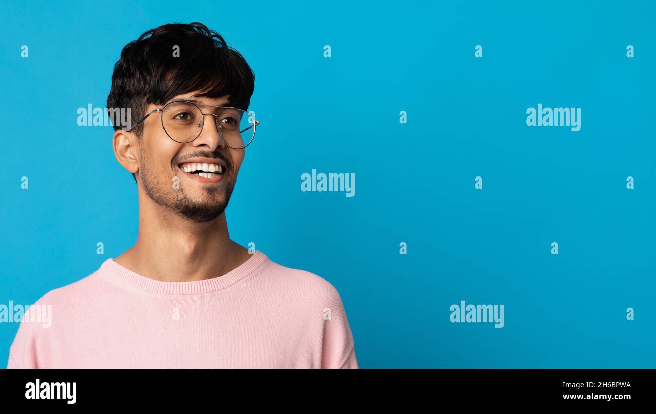 Nahaufnahme Porträt von fröhlich bärtigen indischen Kerl mit Brille posiert über blauen Studio-Hintergrund, Blick auf den Kopierraum, Panorama. Hübscher junger Mann i Stockfoto