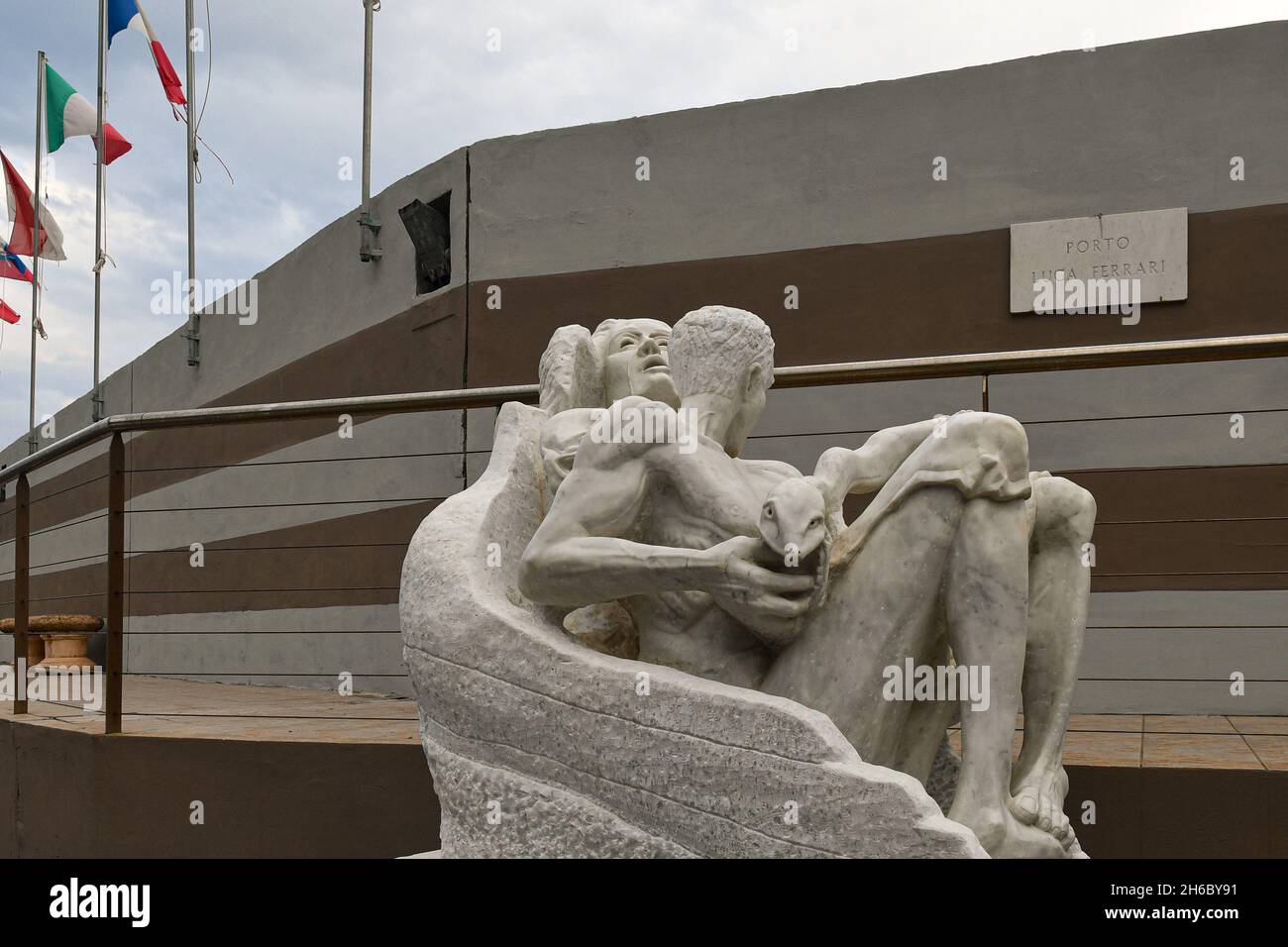 Eine Marmorstatue im Hafen von Porto Luca Ferrari von Alassio mit EU-Flaggen im Hintergrund, Alassio, Savona, Ligurien, Italien Stockfoto