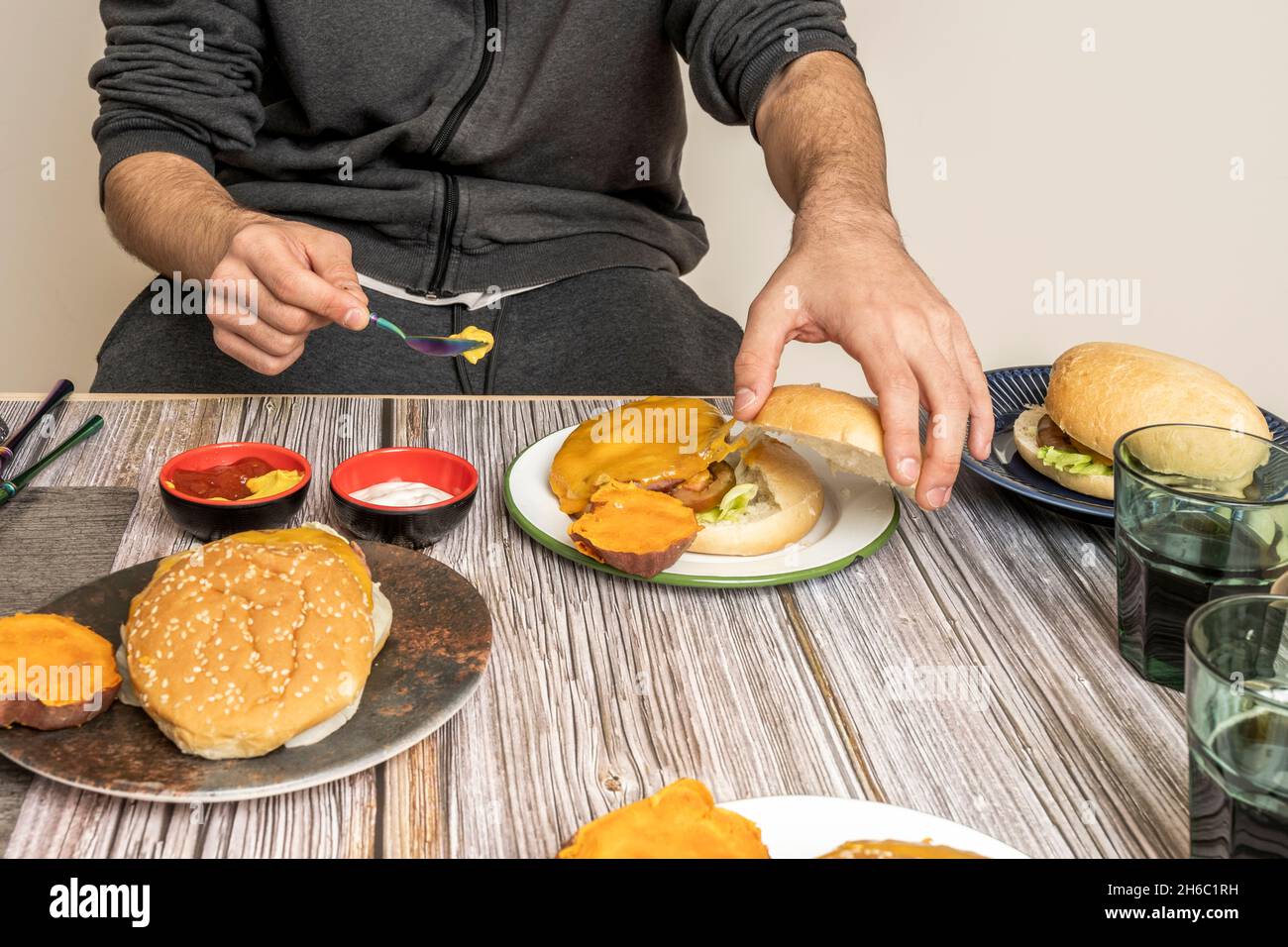 Die Hände des jungen Mannes wählen Saucen aus, die als Gewürz in Kalbsburgern mit Käse und Dorfbrot verwendet werden Stockfoto