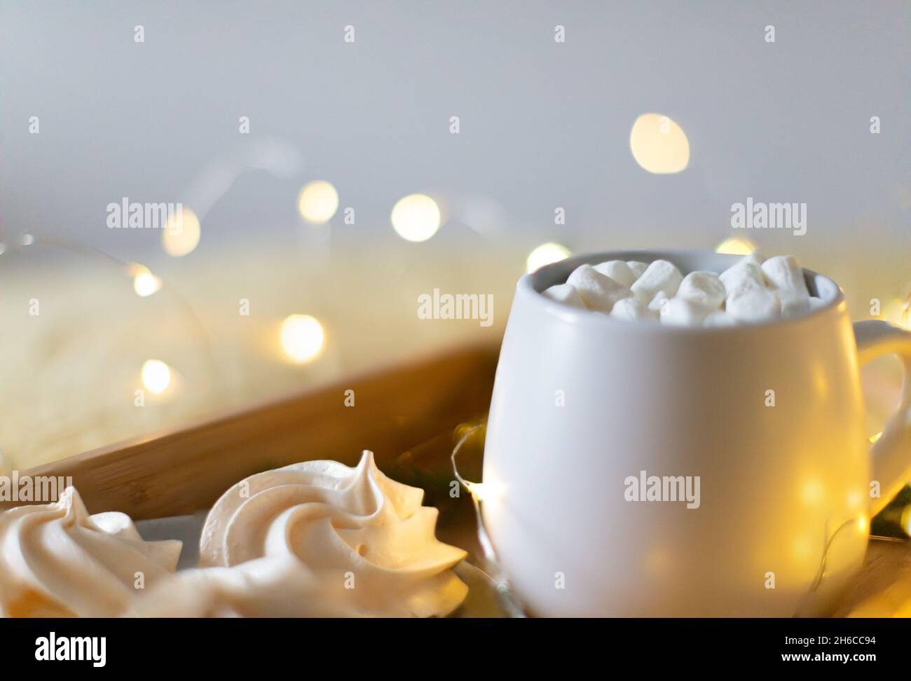 Kakao in einem Becher auf einem Tablett mit Salzwölschen und Baiser. Die Lichter des neuen Jahres im Hintergrund. Stockfoto