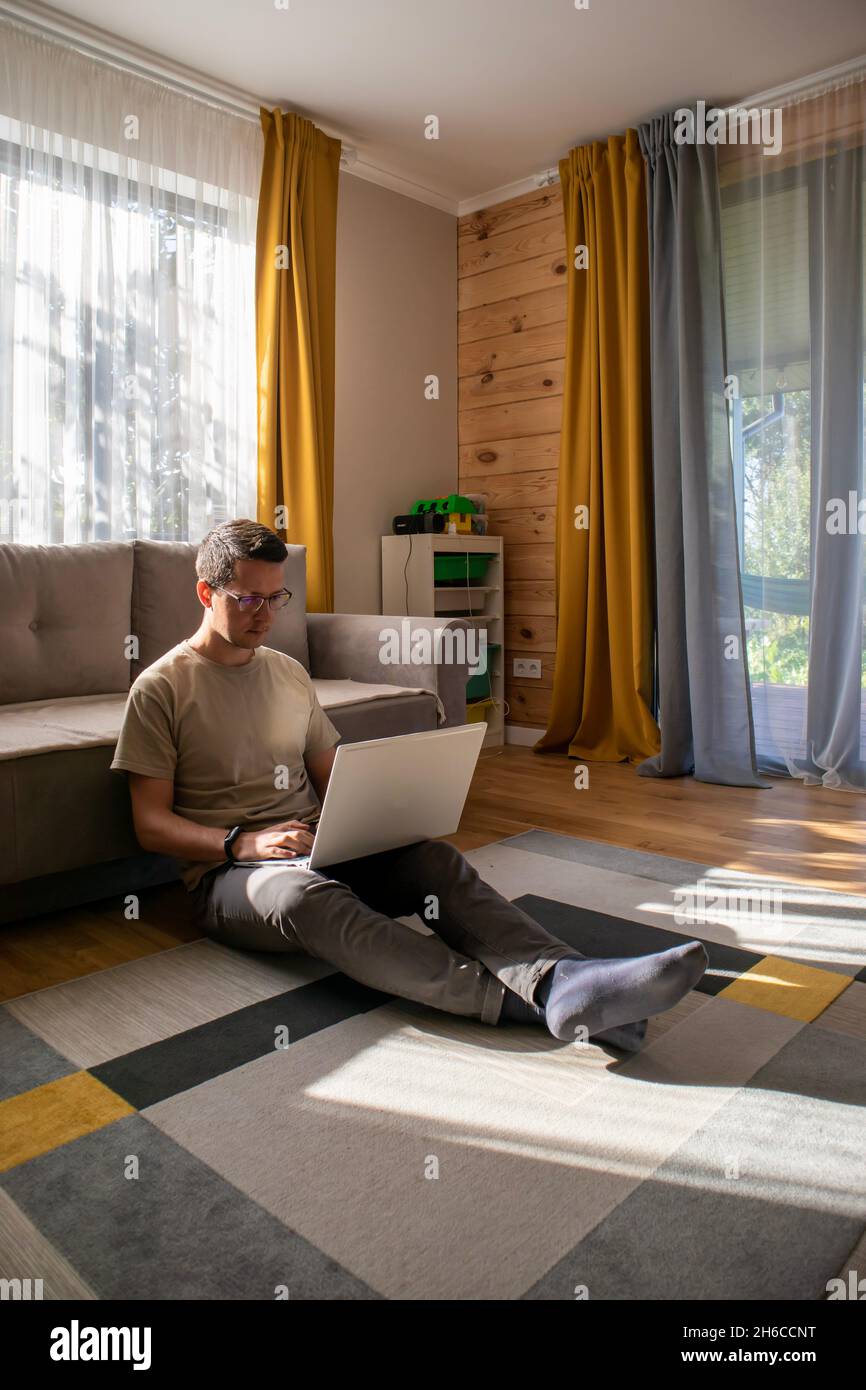 Ein Typ in legerer Kleidung arbeitet auf dem Boden in einer sonnigen Loft-Wohnung Stockfoto
