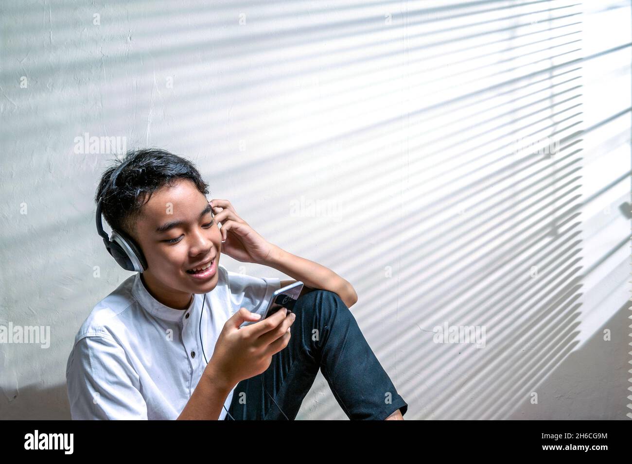 Indonesischer männlicher Teenager, der mit Kopfhörern Musik hört Stockfoto