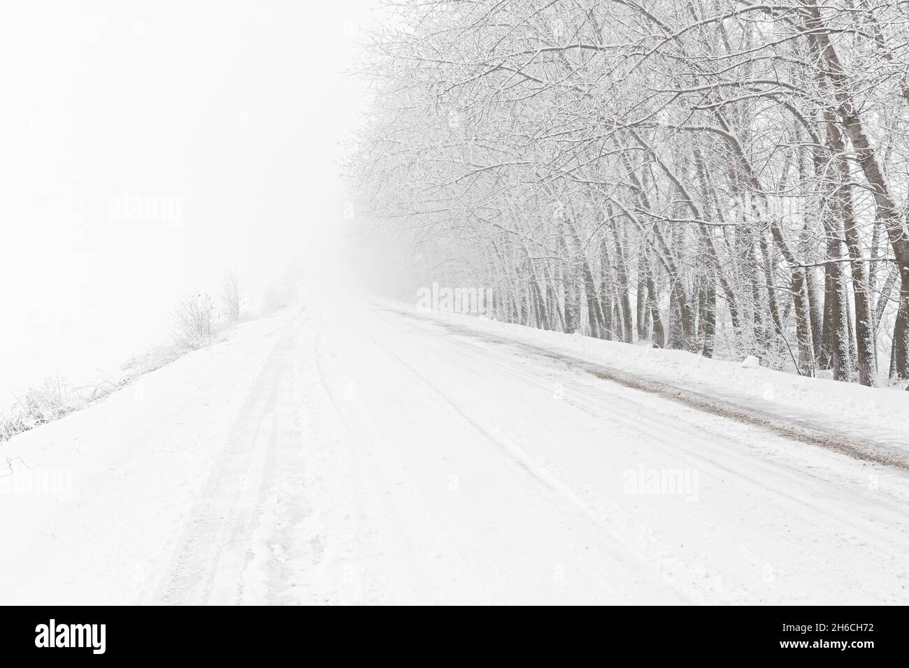 Winterlicher Schneefall auf der Straße. Eine leere Landstraße ohne Autos, bedeckt mit Schneeverwehungen. Reisen Sie bei schlechtem Wetter. Winter wolkige Landschaft mit einer Landstraße. T Stockfoto