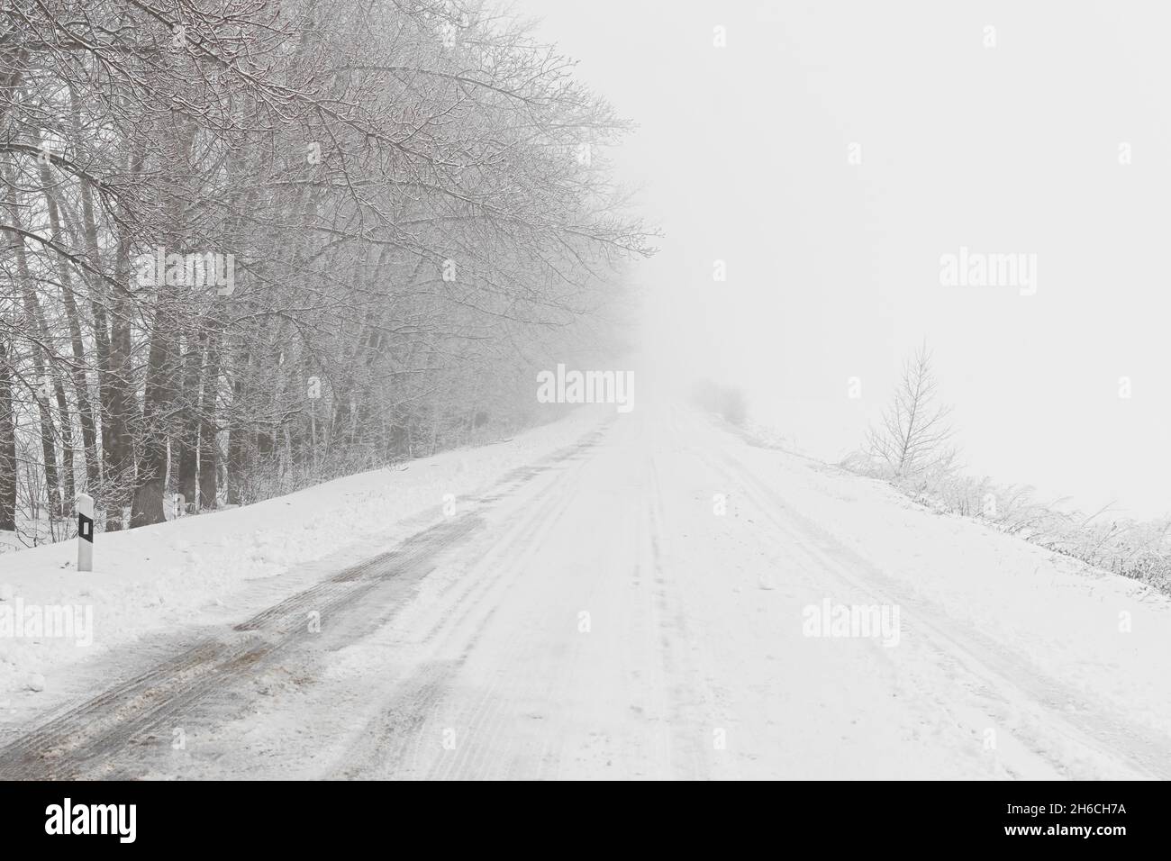 Winterlicher Schneefall auf der Straße. Eine leere Landstraße ohne Autos, bedeckt mit Schneeverwehungen. Reisen Sie bei schlechtem Wetter. Winter wolkige Landschaft mit einer Landstraße. T Stockfoto