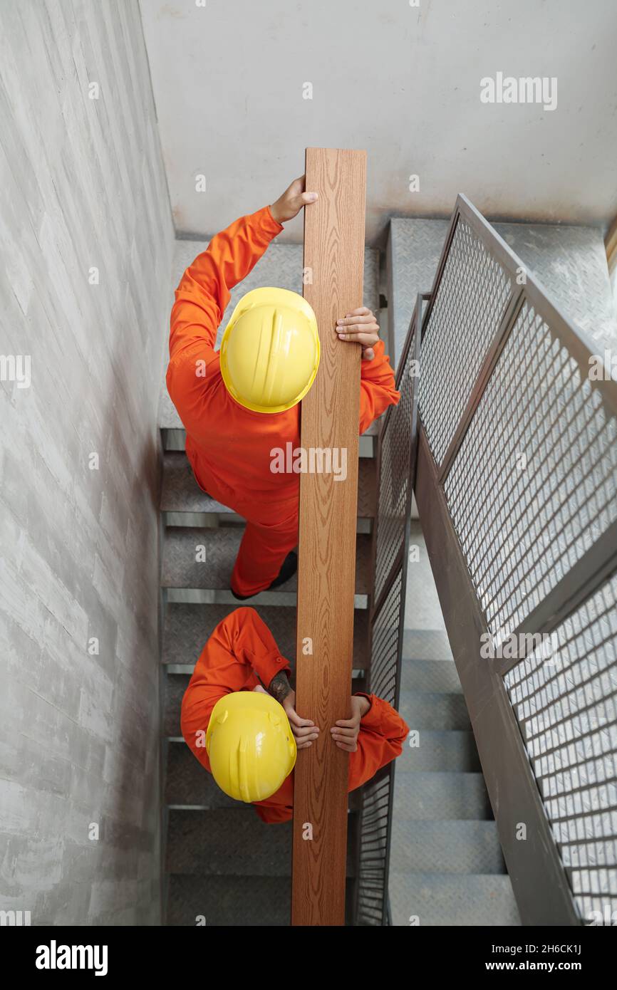 Bauarbeiter in gelben Harthüten, die die Treppe hinauf gehen und lange Holzbrettern tragen, Blick von oben Stockfoto