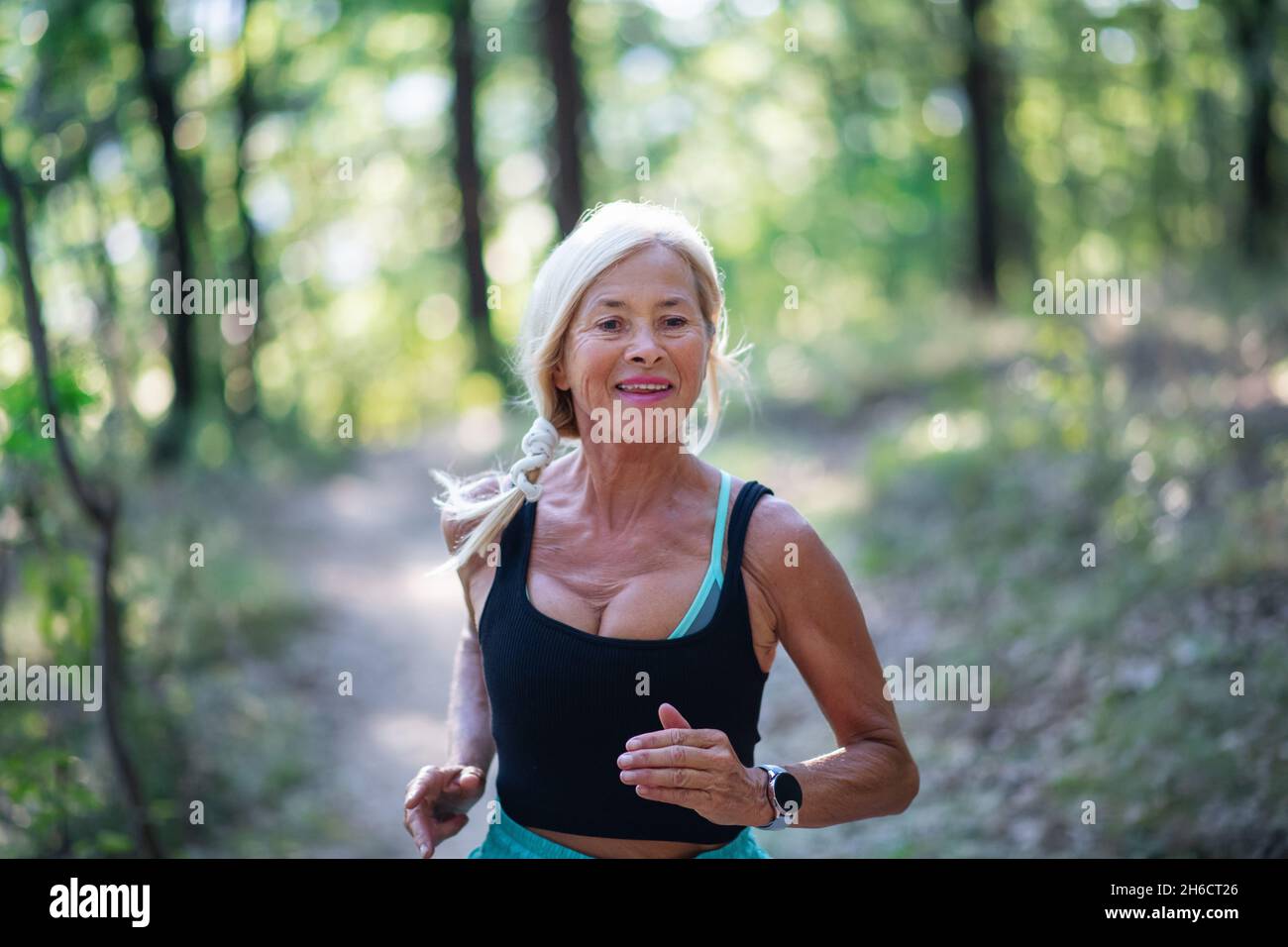 Glückliche aktive ältere Frau joggt draußen im Wald, Taille auf. Stockfoto