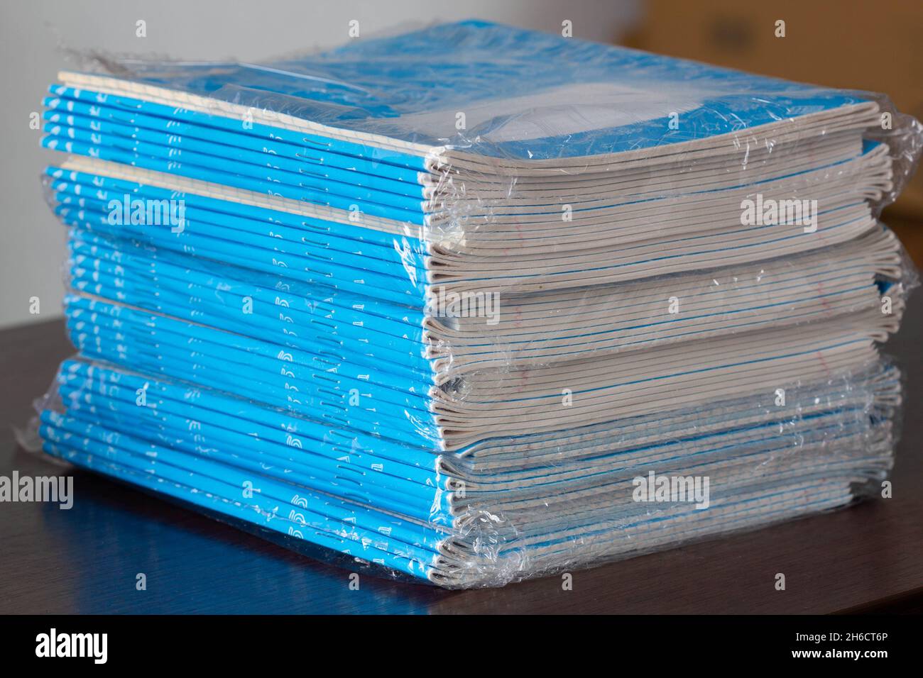 Notebook-Stapel. Eine Packung blauer Schulnotizbücher in Zellophan auf dem Tisch in einem Klassenzimmer. Ein Stapel Übungshefte. Liniertes Papier. Packt kariert Stockfoto