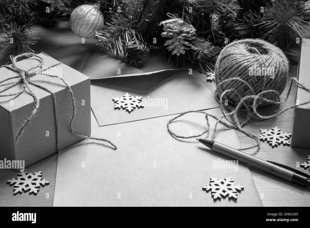 Leeres Blatt Papier, Stift, Geschenke in handgefertigten Schachteln, Garn, künstliche Fichtenzweige und hölzerne Schneeflocken, Draufsicht, schwarz-weiß. Konzept für ec Stockfoto