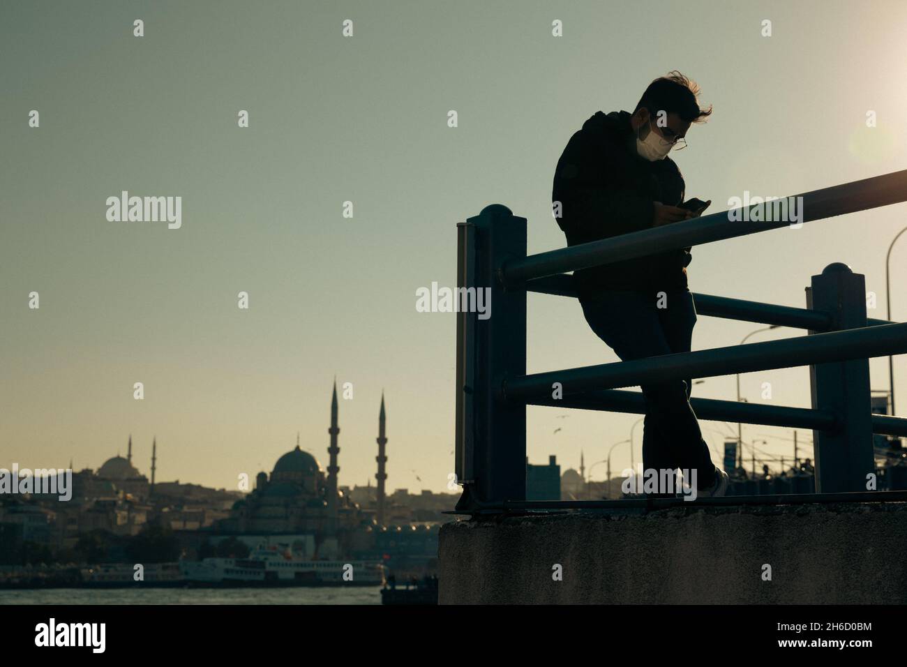 Istanbul, Türkei-12. November 2021: Junger Mann mit Schutzmaske steht auf der Galata-Brücke und überprüft sein Handy. Stockfoto