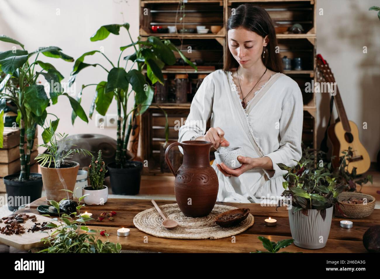 Wasser mit Kakao in den Krug gießen. Zubereitung von zeremoniellem Kakao in einem stimmungsvollen Café im Boho-Stil voller Pflanzen. Frau kocht gesundes Getränk aus Bio Stockfoto