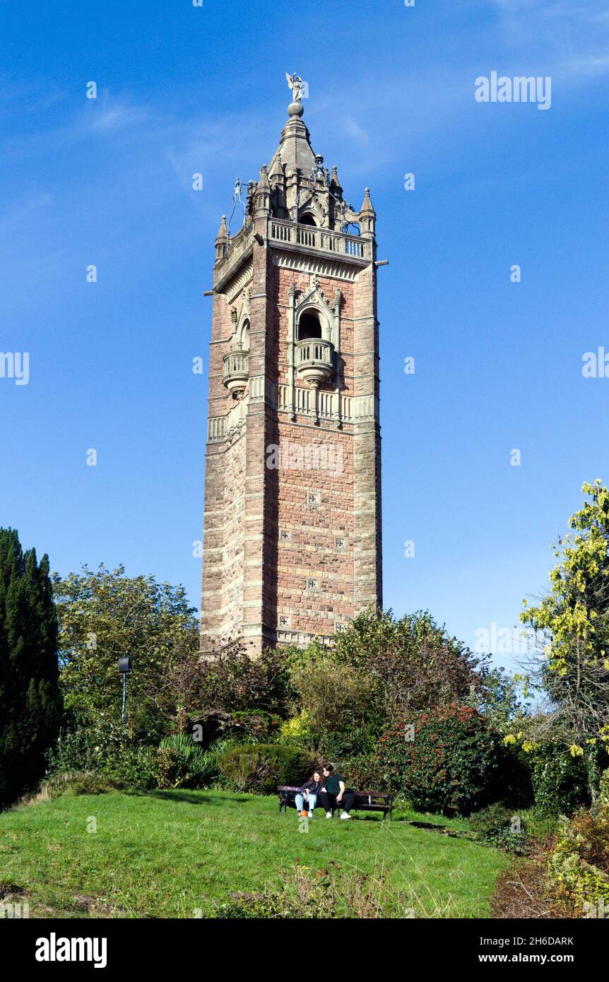 Ein Mann und eine Frau sitzen vor dem Cabot Tower Bristol, in der Stadt und der Grafschaft Bristol; England, Großbritannien, Großbritannien; Sonnenschein und blauer Himmel Stockfoto