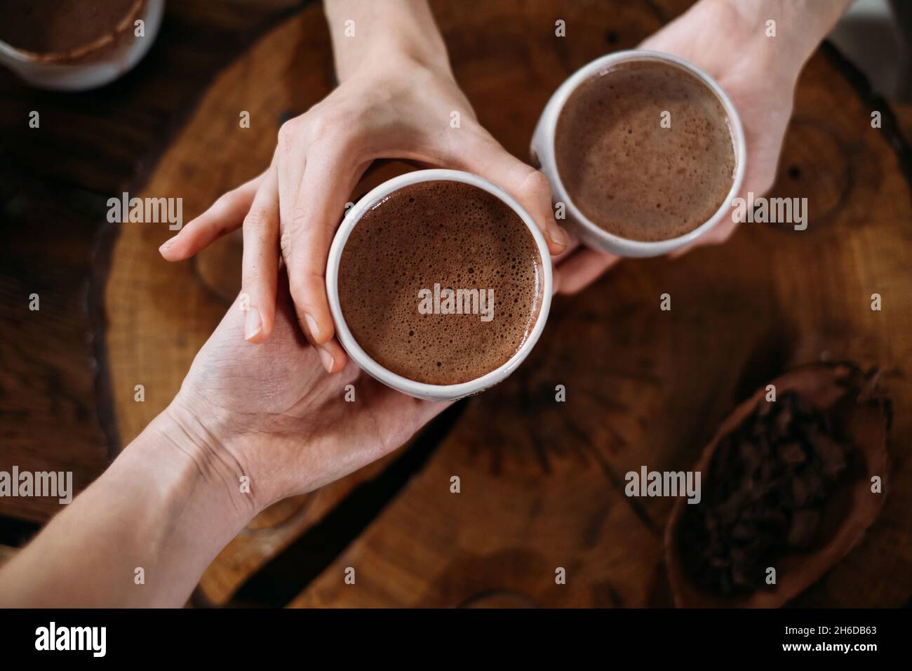 Heißer handgemachter zeremonieller Kakao in weißen Tassen. Frau Hände geben Handwerk Kakao, Draufsicht auf Holztisch. Bio gesundes Schokoladengetränk aus zubereitet Stockfoto