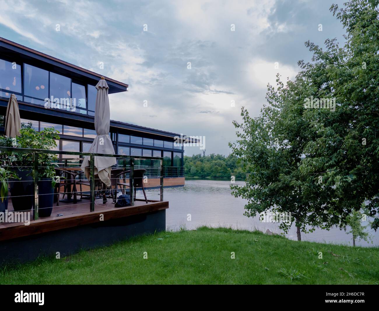Modernes Restaurant mit offener Terrasse und grüner Wiese am linken Ufer des Flusses Dnipro mit Panoramablick über das rechte Ufer mit dem Mutterland-Denkmal. Stockfoto