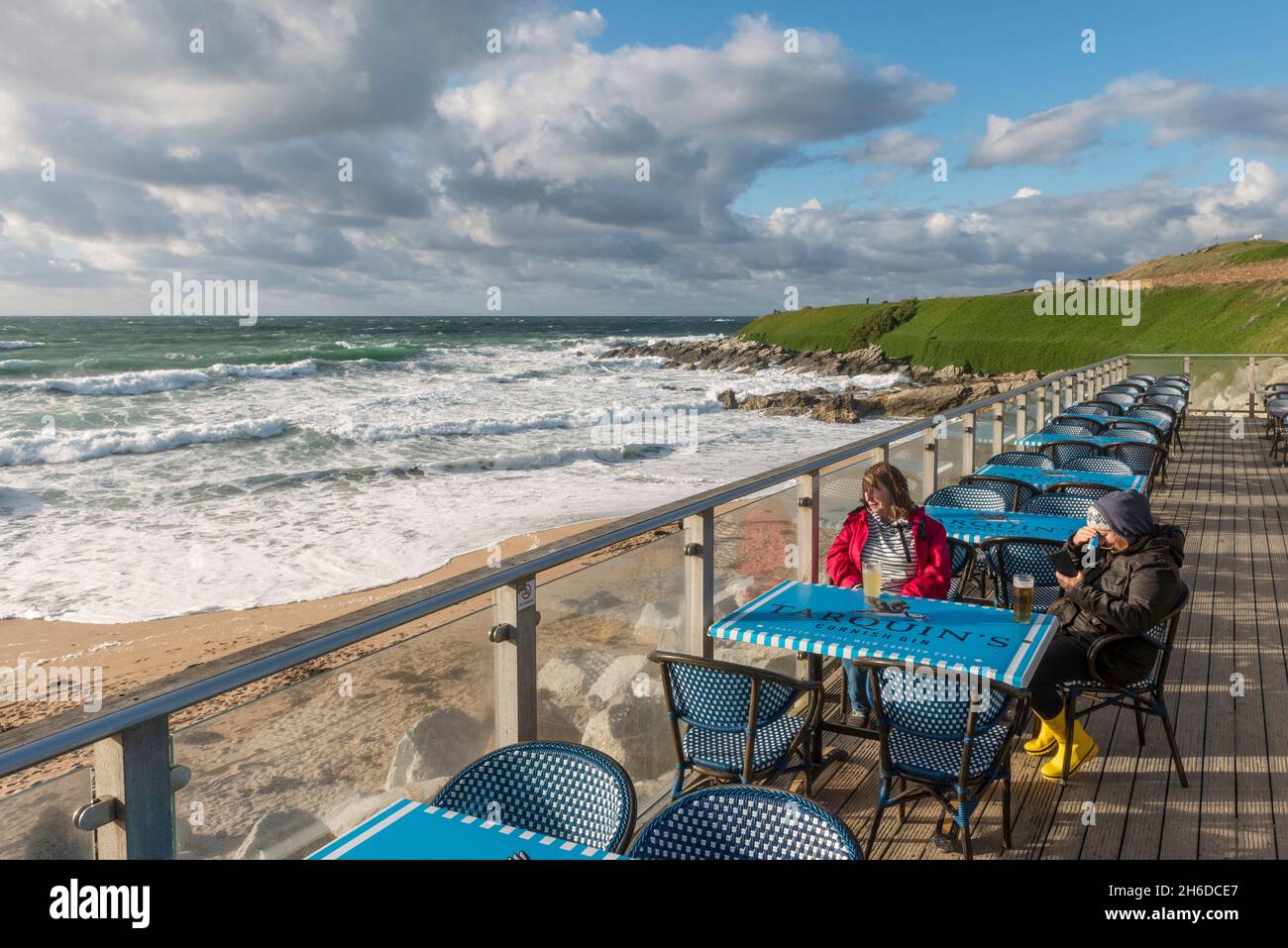 Zwei Menschen trotzen dem kühlen Wetter und sitzen in der Nebensaison in Newquay in Cornwall auf der Terrasse der Fistral Beach Bar. Stockfoto