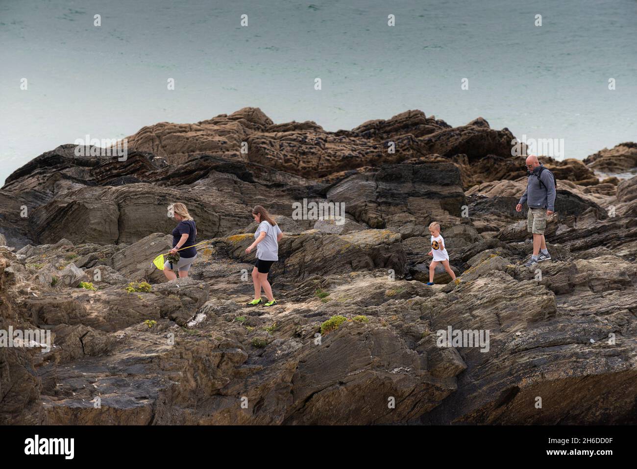 Eine Familie von Urlaubern, die bei Fistral in Newquay in Cornwall vorsichtig auf den Felsen spazieren. Stockfoto