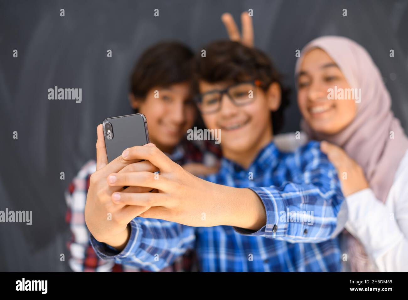 Gruppe von arabischen Teenagern, die Selfie-Fotos auf dem Smartphone mit schwarzer Tafel im Hintergrund machen. Selektiver Fokus Stockfoto