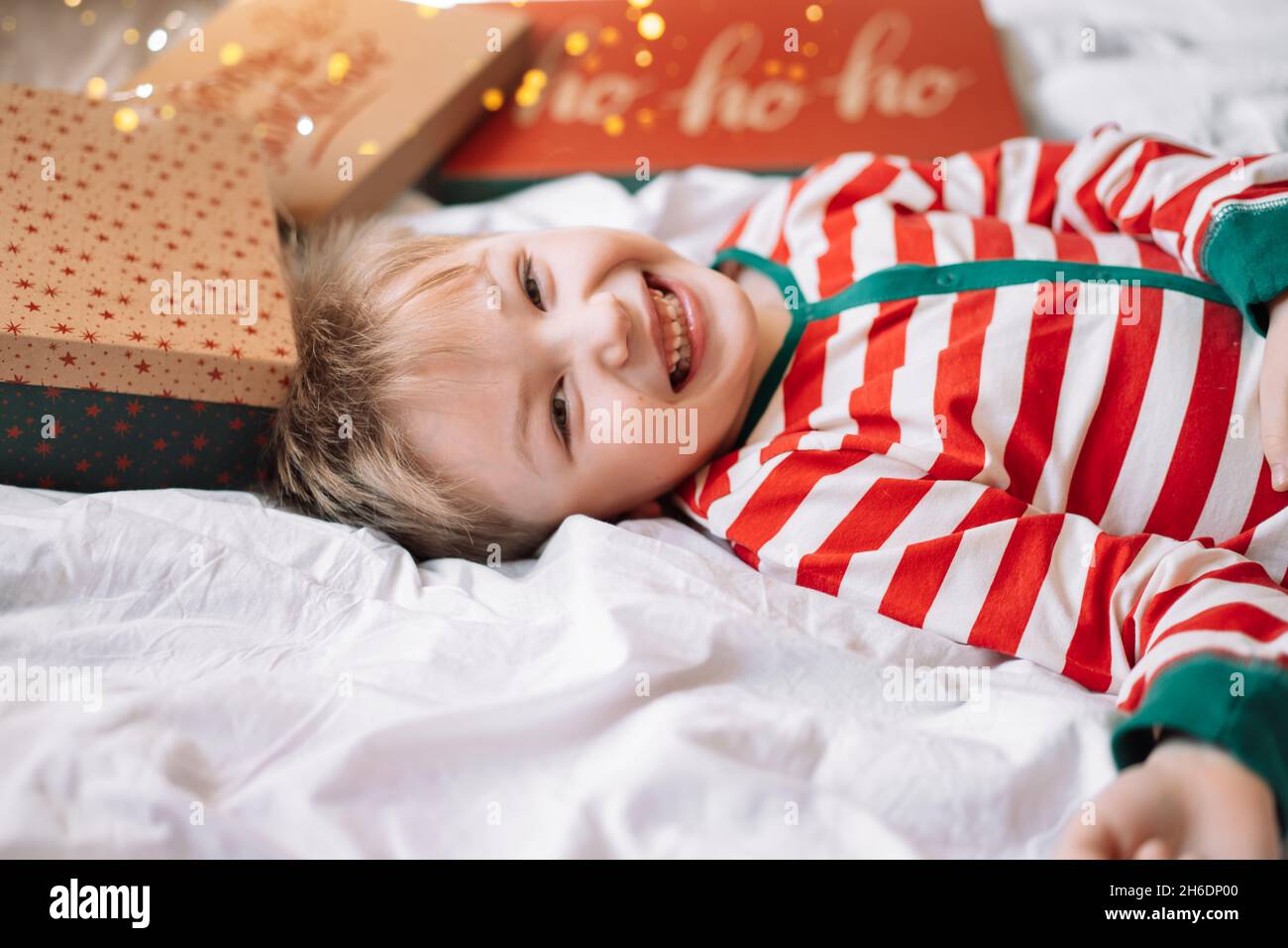 Boy im gestreiften Schlafanzug liegt mit Geschenkkartondeckeln und Girlande auf dem Bett Stockfoto