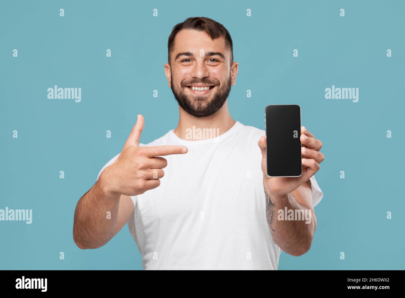 Lächelnd schöner reifer europäischer Mann zeigt Finger auf Smartphone mit leerem Bildschirm Stockfoto