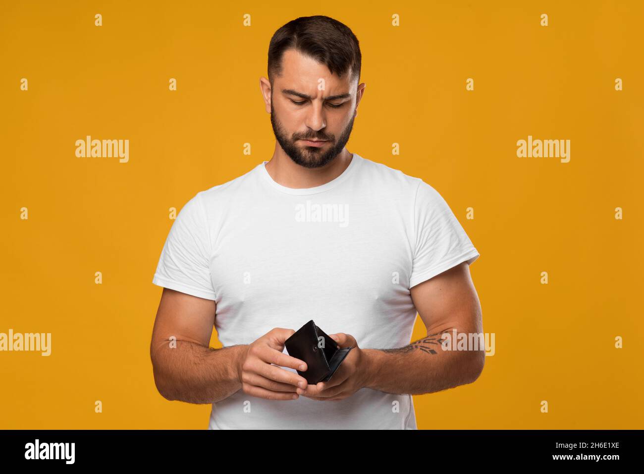 Enttäuschender trauriger europäischer Männerlook mittleren Alters bei leerer Brieftasche, isoliert auf gelbem Hintergrund Stockfoto
