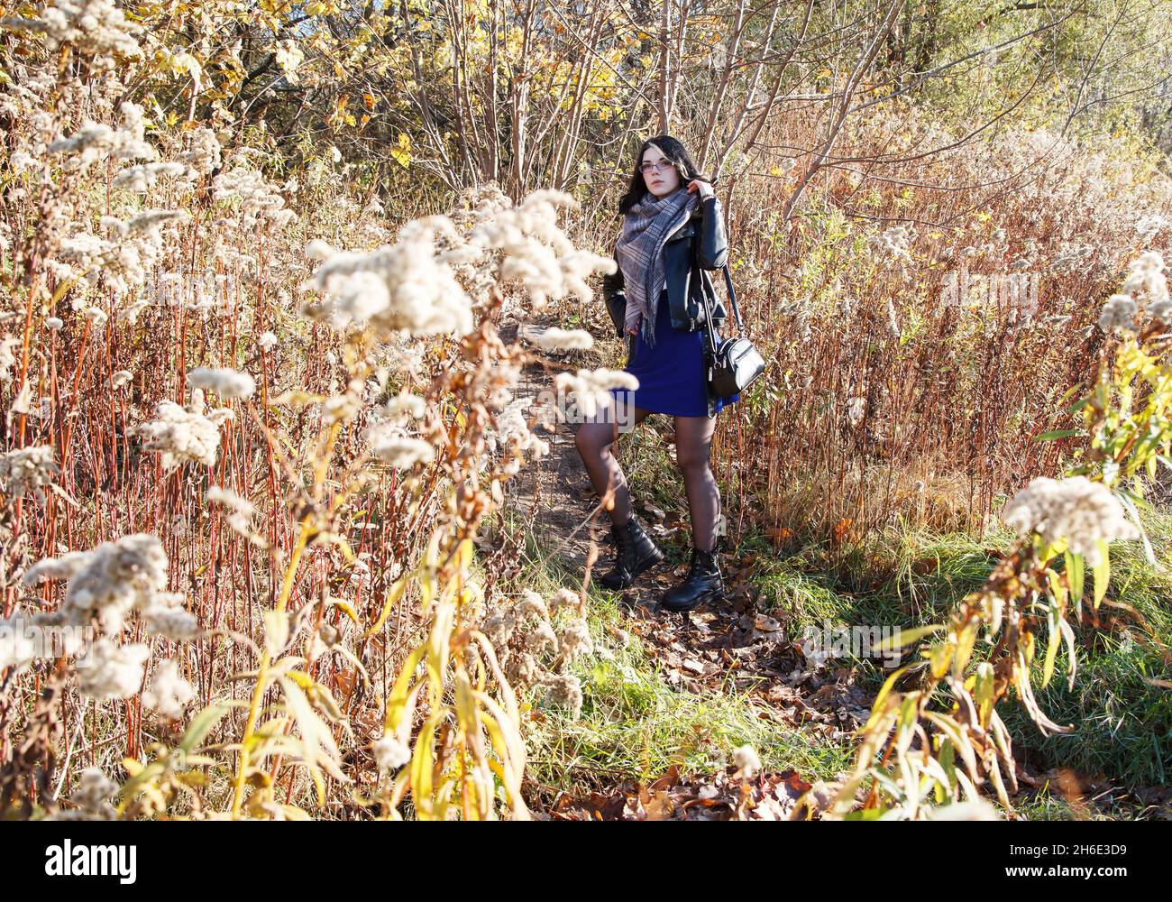 Junge Brünette Mädchen in schwarzer Jacke und blauem Kleid steht auf dem Weg im Wald an sonnigen Herbsttag Stockfoto