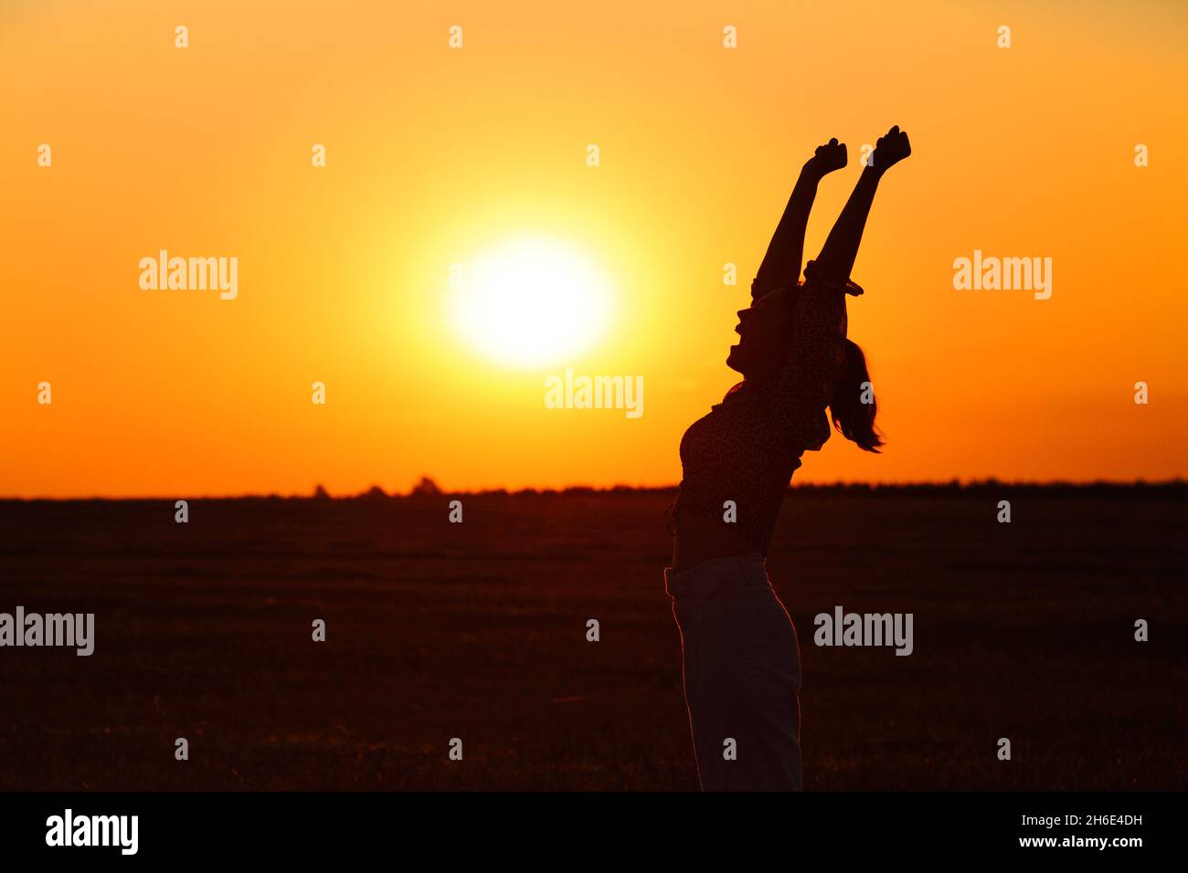 Profil einer aufgeregten Frau, die die Arme hebt und den Erfolg bei Sonnenuntergang feiert Stockfoto