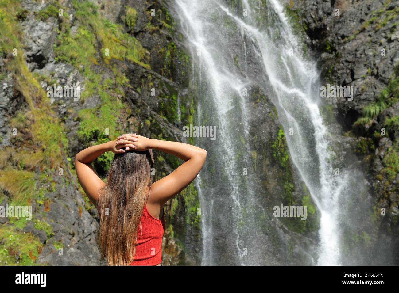 Rückansicht einer Frau, die über einen Wasserfall im Berg nachdenkt Stockfoto