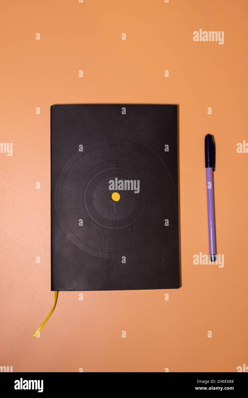 Schwarzes Notizbuch mit violettem Stift auf orangefarbenem Hintergrund Stockfoto
