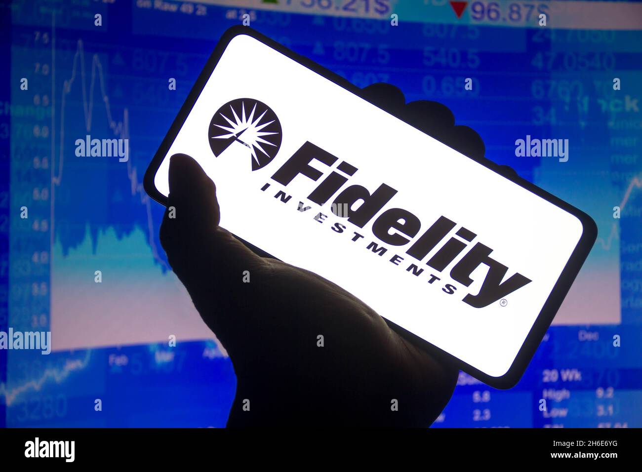 In dieser Abbildung wird das Fidelity Investments-Logo auf einem Smartphone-Bildschirm und im Hintergrund ein Börsendiagramm angezeigt. Stockfoto