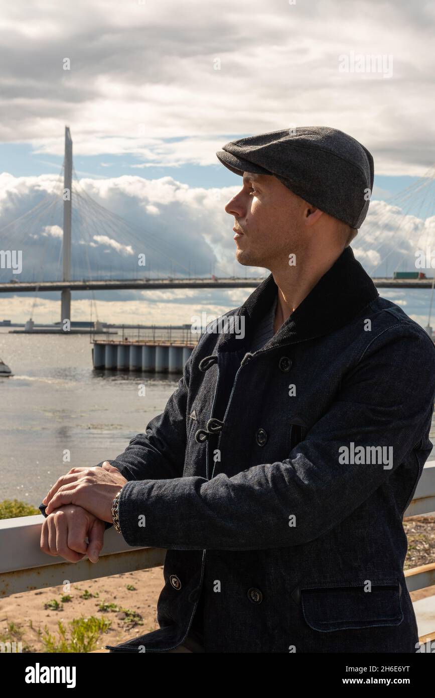 Ein Mann in einem Mantel und einer Mütze auf dem Hintergrund der Brücke. Hochwertige Fotos Stockfoto