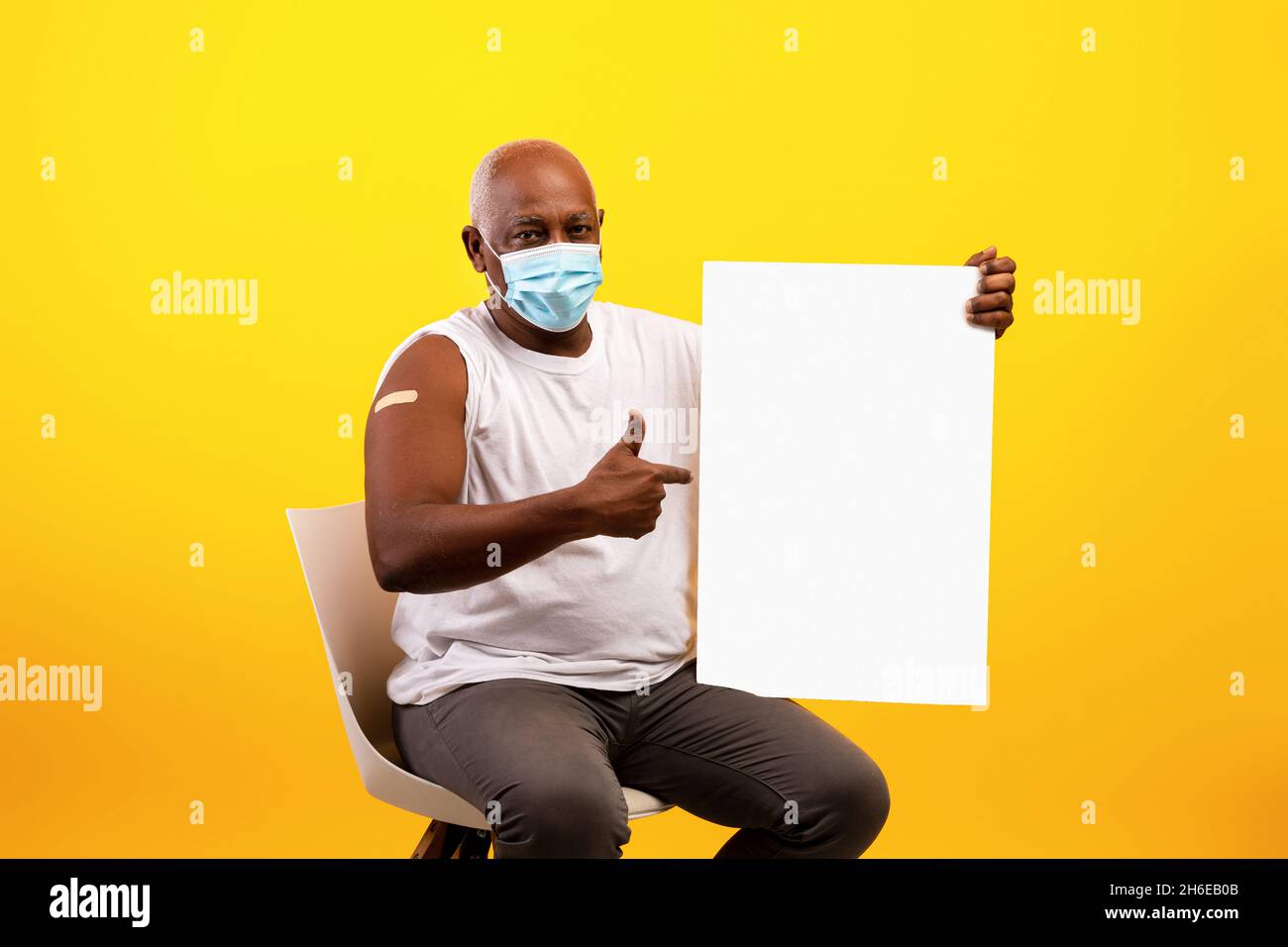 Coronavirus-Impfung. Älterer schwarzer Mann in einer Anti-Covid-Maske mit Haftverband, der auf ein Papierbanner mit Mockup zeigt Stockfoto