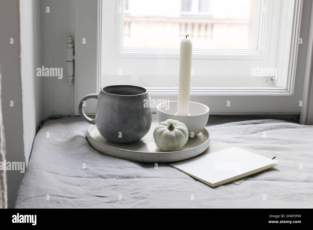 Stillleben im Herbst. Weißer kleiner Kürbis, eine Tasse Kaffee und ein leeres Grußkartenmockup am Fenster. Kerze mit weißem keramischen Kerzenhalter. Moody Fall Stockfoto Stillleben im Herbst. Weißer kleiner Kürbis, eine Tasse Kaffee und ein leeres Grußkartenmockup am Fenster. Kerze mit weißem keramischen Kerzenhalter. Moody Fall Stockfoto