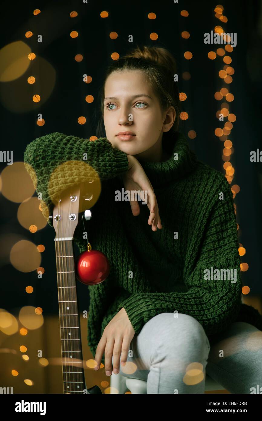 Ein schönes Teenager-Mädchen schaut träumerisch zur Seite, lehnt sich an den Hals einer Gitarre. Ruhiges, ruhiges Gesicht eines Teenagers, ausdrucksstarke Augen, ein Blick auf Stockfoto