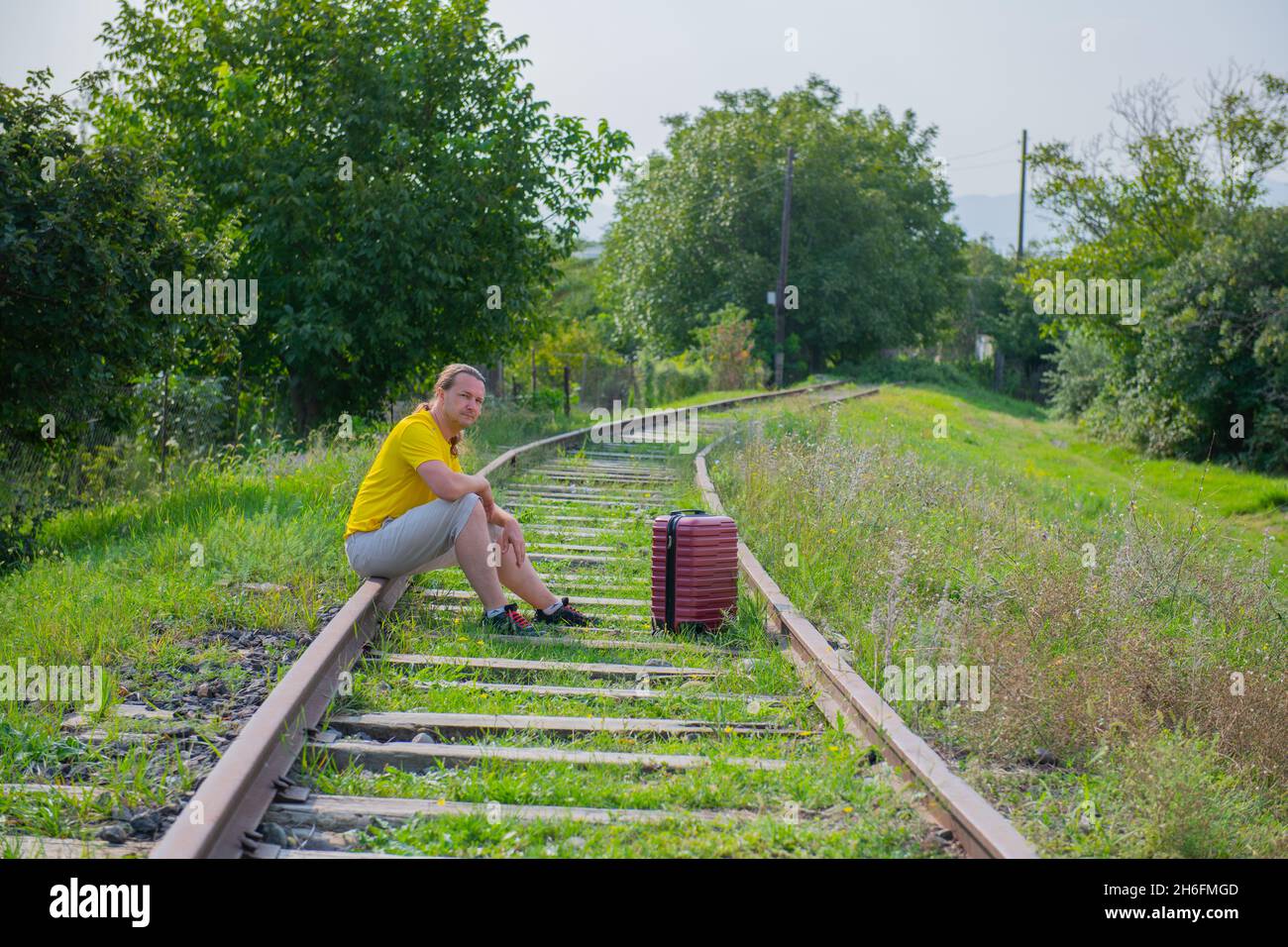 Ein Mann mit einem roten Koffer auf der Eisenbahn sitzt Stockfoto