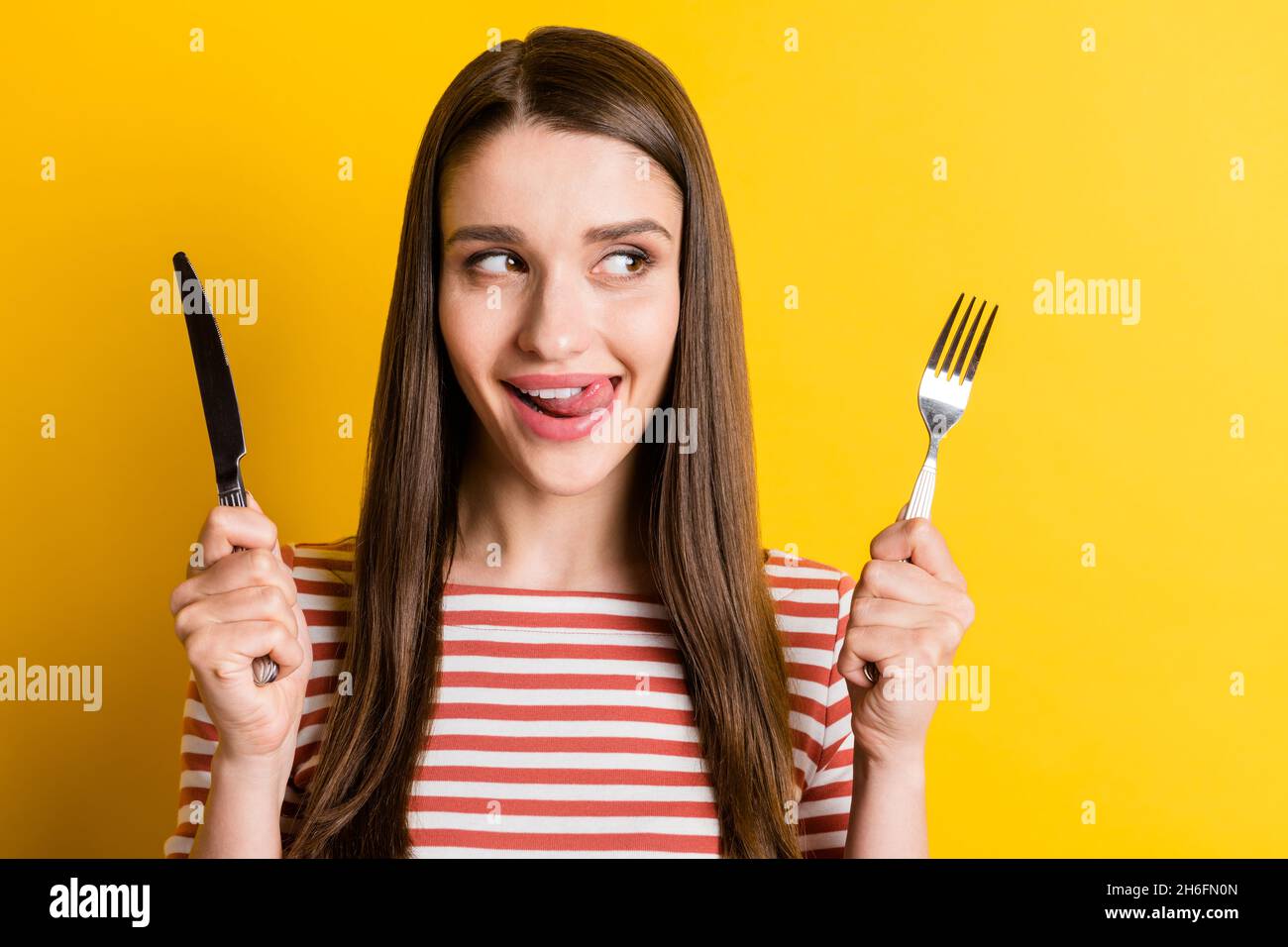 Portrait von attraktiven fröhlichen Mädchen hungrig halten Besteck lecken Lippe isoliert über helle gelbe Farbe Hintergrund Stockfoto