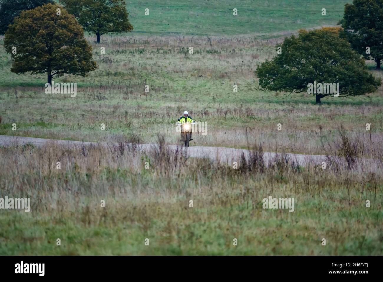 Ein Motorradfahrer (Biker) in einer gelben Jacke, der mit seinem Motorrad auf einem Steinweg auf der Salisbury Plain, Wiltshire, fährt Stockfoto